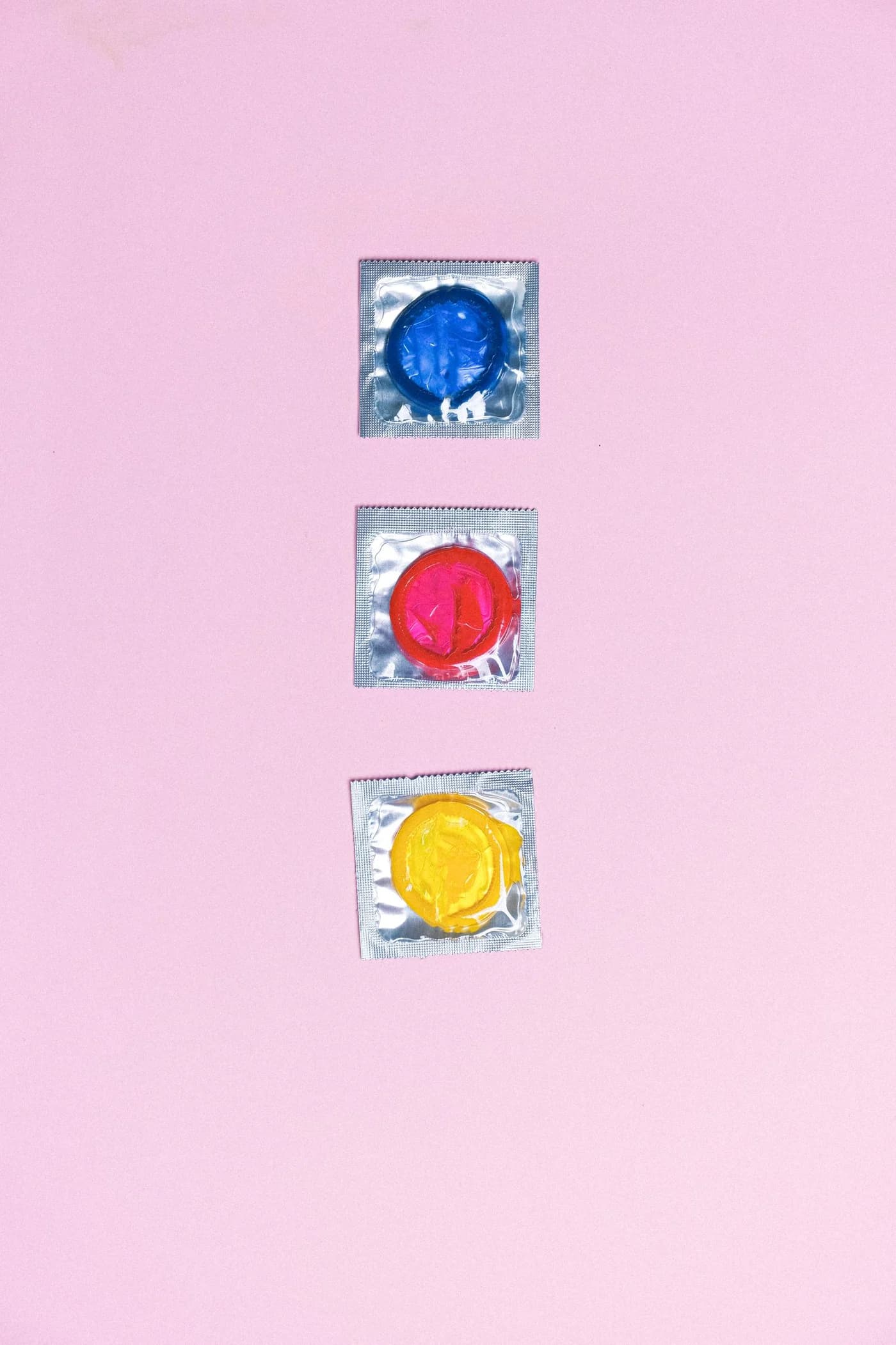 Blue, red and yellow individually wrapped condoms arranged on pink