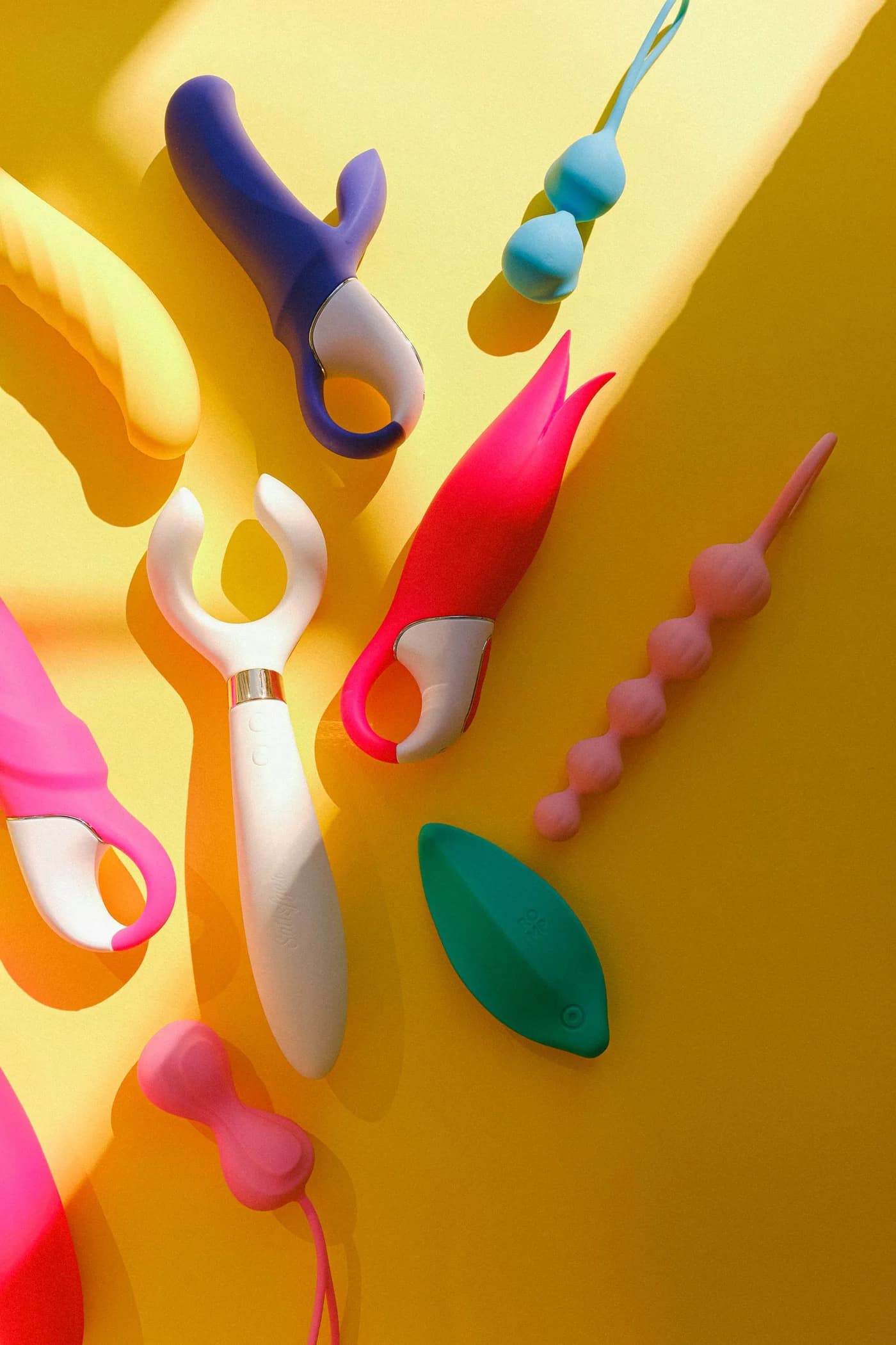 Colourful vibrators, intimate beads and accessories arranged on yellow